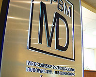 Srebrny metalowy szyld z wypukłymi
granatowymi podświetlanymi literami dla Wrocławskiego Przedsiębiorstwa Budownictwa Mieszkaniowego