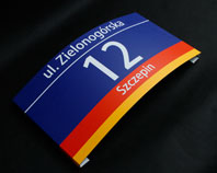Aluminiowa tablica informująca o adresowa 
zaginana po łuku 
z numerem nazwą ulicy i dzielnicy 
we Wrocławiu